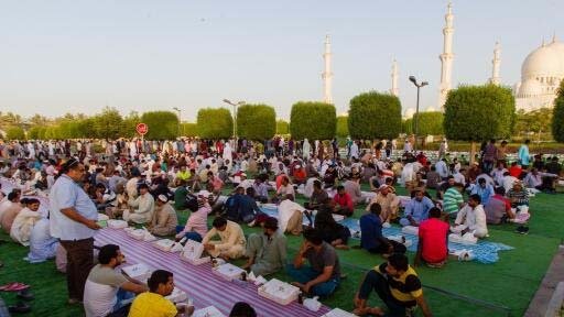 Muslims gathering in Dubai for an Iftar meal in a mosque, sharing traditional Ramadan dishes, including dates and wate