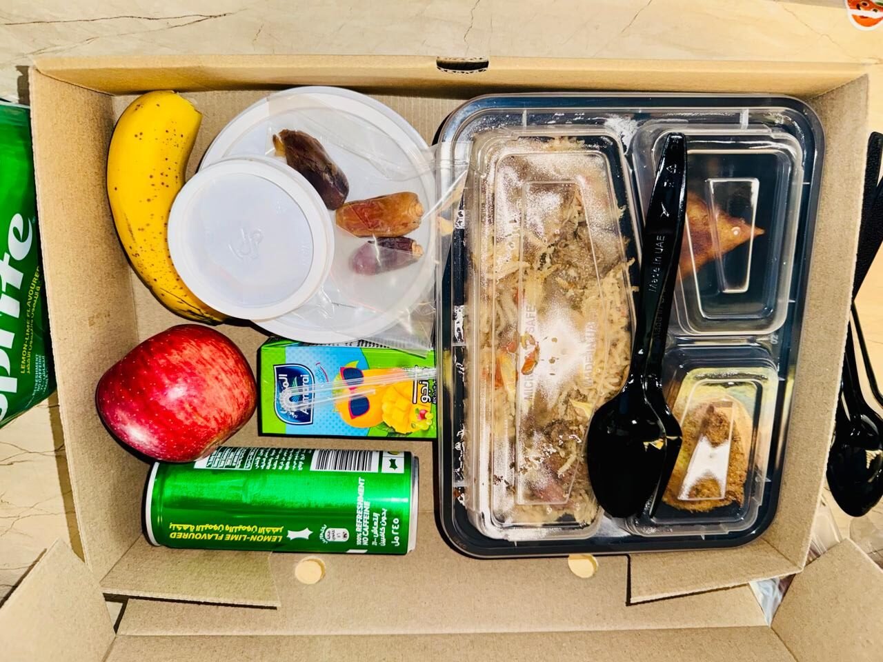 A meal box containing rice, chicken, fruits, drinks, and dates, designed for convenient office lunch catering