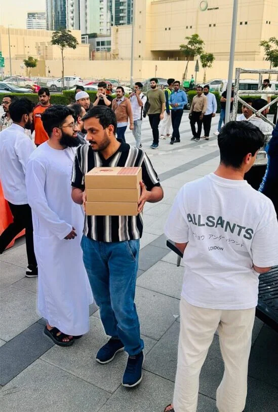 Volunteers distributing charity meal boxes to men outside a mosque (Masjid) after Friday prayer, symbolizing essential community support.